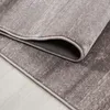 A close-up view of a folded gray rug with a textured, mottled pattern, resting on a light-colored wooden floor. Podgląd zdjęcia produktu