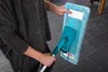 A person is holding a mop with a blue cleaning pad. Produktbild-Vorschau