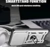 A silver phone case with a ring holder is placed on a textured surface, with a blurred laptop and headphones in the background. Produktbild-Vorschau