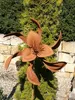 A rusted metal flower sculpture in a garden setting, with a stone wall and greenery in the background. Produktbild-Vorschau