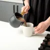 A person is pouring hot chocolate from a pot into a mug. Náhled obrázku produktu