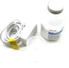 A white power adapter with a coiled white cord, a small clear plastic cup, and a white bottle of sea salt are arranged on a white background. Produktbild-Vorschau