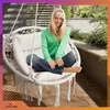 A woman is sitting in a white hanging chair on a balcony. Voir les images du produit