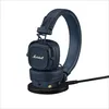 A pair of blue Marshall headphones are placed on a black charging base, with a black cable connected. Produktbild-Vorschau