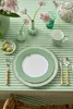 A table setting with a green and white striped tablecloth, featuring a plate, cutlery, a mug, and decorative items. Produktbild-Vorschau