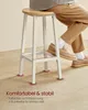 A person's legs and feet are shown resting on a bar stool in a room. Produktbild-Vorschau