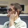 A man wearing sunglasses and in-ear headphones, smiling and touching one of the headphones. Anteprima dell’immagine prodotto