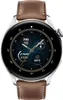 A close-up, front-facing view of a smartwatch with a brown leather strap and a metallic silver casing. The watch face displays the time, date, battery percentage, step count, and weather information. Anteprima dell’immagine prodotto