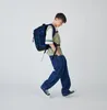 A young person wearing a backpack and casual clothing walks with their hands in their pockets. Produktbild-Vorschau