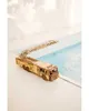 A wooden model fire truck with an extended ladder sits on a white surface next to a pool of blue water. Produktbild-Vorschau