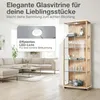 A glass display cabinet filled with items, placed in a living room setting next to a sofa. Produktbild-Vorschau