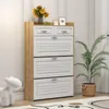 A white and natural wood shoe cabinet with decorative items on top, placed in a room with a plant and a decorative white sculpture. Náhľad obrázku produktu