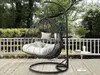 A hanging chair with cushions on a wooden deck, with a white railing and trees in the background. Náhled obrázku produktu
