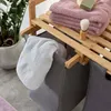 A close-up of a bamboo laundry basket with two gray fabric bins, one holding a white towel. Pink towels and soap are on the top shelf. Produktbild-Vorschau