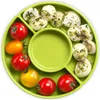 A top-down view of a green divided plate filled with cherry tomatoes and mozzarella balls seasoned with herbs and pesto. Produktbild-Vorschau