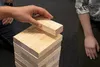 A hand is carefully removing a wooden block from a Jenga tower. Produktbild-Vorschau