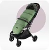A green stroller footmuff with a fur-lined hood is attached to a stroller. The background is a gradient of white to light purple. Náhľad obrázku produktu