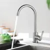 A kitchen faucet with water running into a sink, with some vegetables and containers in the background. Produktbild-Vorschau