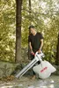 A man is using a leaf blower in an outdoor setting with trees and fallen leaves. Produktbild-Vorschau
