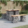 An outdoor patio setting with a gabion table and benches made of stones and wood, with a wooden fence and greenery in the background. Náhled obrázku produktu