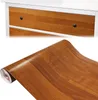 A roll of wood-grain contact paper is shown in front of a dresser with similar wood-grain drawers. Produktbild-Vorschau