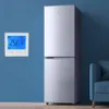 A digital thermostat is mounted on a blue wall next to a silver refrigerator. Produktbild-Vorschau