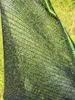 A close-up view of a black shade net with green trim, showing its woven texture. The background is blurred green foliage. Produktbild-Vorschau