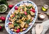 A platter of grilled halloumi cheese with potatoes and radishes, dressed with a green herb sauce, is presented on a wooden table. Produktbild-Vorschau