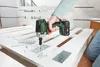 A person is using a cordless impact driver to attach a metal plate to a white wooden structure, likely a pallet or furniture. Podgląd zdjęcia produktu