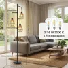 A floor lamp with three lights is shown in a living room setting next to a sofa and coffee table. Produktbild-Vorschau