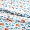 A close-up view of a white fabric with a repeating pattern of orange deer and blue foliage. Produktbild-Vorschau