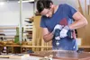 A man is using a cordless drill to drill into a wooden surface in a workshop. Voir les images du produit