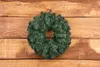 A green Christmas wreath is centered on a wooden plank background. Náhled obrázku produktu
