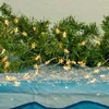 A close-up of a string of star-shaped LED lights woven through artificial pine garland, resting on a blue surface with a snowy texture. Produktbild-Vorschau