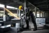 A construction worker is using an angle grinder to cut metal ductwork in an unfinished building. Náhľad obrázku produktu