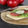 A sandwich with cheese, lettuce, tomato, and cucumber on a wooden cutting board, with two tomatoes in the background and cutlery. Produktbild-Vorschau