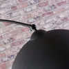 A close-up shot of a black metal lamp arm and shade against a brick wall. Produktbild-Vorschau