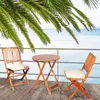 A wooden bistro set with two chairs and a round table on a wooden deck overlooking the ocean, with palm fronds in the foreground. Náhľad obrázku produktu