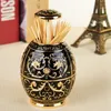 A decorative black and gold toothpick holder is shown on a table with books and a miniature Eiffel Tower in the background. Náhled obrázku produktu