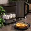 A breakfast scene on a kitchen counter, featuring an egg cooker, a kettle, and toast. Voir les images du produit