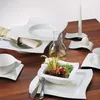 A beautifully set dining table with modern white porcelain plates, cutlery, a carafe of oil, and a candle with an egg holder. Produktbild-Vorschau
