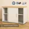 A white cabinet with sliding doors and a wooden top, placed on a wooden floor against a light wall. Several certification logos are displayed at the top, and a text overlay with a checkmark is at the bottom. Produktbild-Vorschau