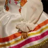 A close-up view of a doll's dress with embroidered flowers and colorful ribbon trim. Náhled obrázku produktu