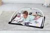 A baby is playing on a black and white play mat with hanging toys. Náhled obrázku produktu