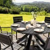 A round, black garden table set with plates and cups, set on a wooden deck with a scenic, green landscape in the background. Produktbild-Vorschau
