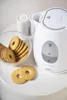 A white electric kettle with a glass water level indicator sits on a white surface next to a bowl of biscuits and two salt shakers. Voir les images du produit