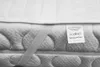A close-up view of a quilted mattress protector with a care label attached. Náhled obrázku produktu