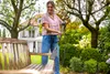 A woman is cleaning a wooden bench in a garden with a pressure washer. Produktbild-Vorschau