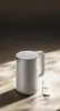 A white electric kettle and a small glass of water are placed on a textured surface with dramatic lighting. Náhľad obrázku produktu