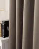A close-up view of taupe-colored curtains, with a book and part of a lamp visible on a white surface to the left. Produktbild-Vorschau